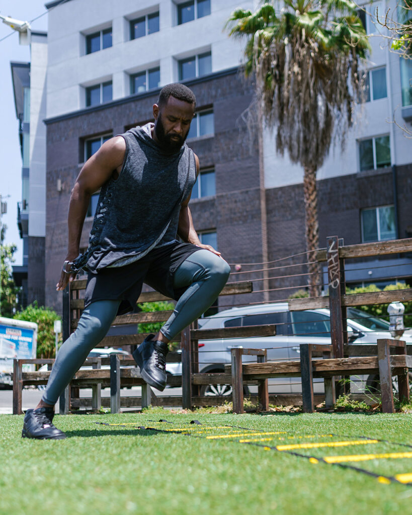 Black Man in Sportswear Exercising on Lawn with Exercise Ladder